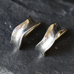 May include: A pair of silver earrings with a wavy, curved design. The earrings are made of smooth, polished metal.