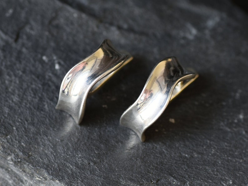 May include: A pair of silver earrings with a wavy, curved design. The earrings are made of smooth, polished metal.