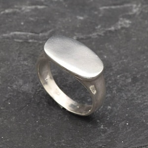 Op de afbeelding: Een zilveren ring met een gladde, ovale bovenkant. De ring is gemaakt van metaal en heeft een gepolijste afwerking.