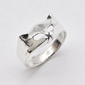 May include: A silver ring with a cat face design. The ring is made of smooth, polished metal and has a simple, modern style.