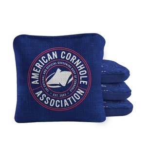 May include: A set of four blue cornhole bags with the American Cornhole Association logo. The logo is a white silhouette of a cornhole board with the text "American Cornhole Association" and "The Original and Official Governing Body of Cornhole" around the outside of the logo. The text "Est. 2003" is below the logo.