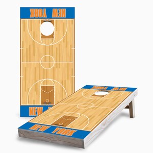 May include: A wooden cornhole game with a basketball court design. The boards are painted with a blue and orange color scheme and feature the text "NEW YORK".