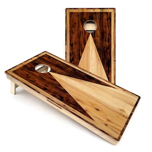 May include: Two wooden cornhole boards with a triangular design. The boards are made of dark wood with light wood accents. The boards are set up for a game of cornhole.