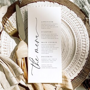 Może przedstawiać: Formalne nakrycie stołu z białą kartą menu z napisem "the menu" w eleganckim skrypcie. Menu zawiera przystawki, przystawki, dania główne i desery. Złoty widelec i nóż umieszczone są na białym i brązowym talerzu, z beżową serwetką.