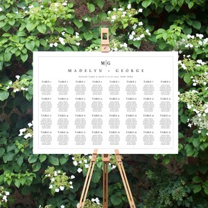 May include: A white wedding seating chart with black text. The chart is titled "Madelyn + George" and lists table numbers from 1 to 32. Each table has a list of names.