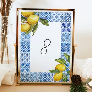 May include: A gold-framed table number card with a blue and white tile pattern. The card features a watercolor illustration of lemons and flowers. The number 8 is printed in black on the card.