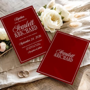 May include: Burgundy wedding invitations with gold text, featuring the names "Scarlett & Richard" and wedding details. The invitations are accompanied by white flowers and gold wedding rings.