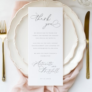 Könnte beinhalten: Eine formelle Tischdekoration mit einem weißen Teller, goldenem Besteck und einer Karte mit der Aufschrift "Danke". Die Karte enthält auch die Namen "Antoinette und Mitchell" und das Datum "07 12 2022". Zarte rosa Blumen und eine rosa Serviette.