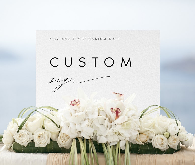 May include: A white sign with black text that reads "5"x"7 and 8"x"10" Custom Sign" and "CUSTOM sign" in cursive. The sign is sitting on a table with white flowers.