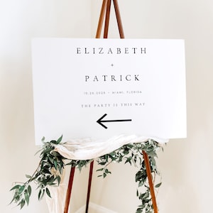 May include: White wedding sign with black text that reads "Elizabeth + Patrick 10.26.2026 - Miami, Florida The Party is This Way" with a black arrow pointing left.