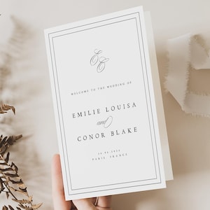 Può includere: Un invito di nozze bianco con bordo e testo neri. L'invito recita "Benvenuti al matrimonio di Emilie Louisa e Conor Blake" con la data e il luogo, Parigi, Francia.