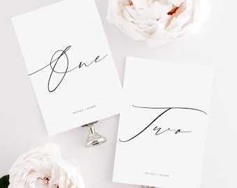 May include: Two white cards with black calligraphy, one says "One" and the other says "Two". Both cards have the text "Nicole + Henry" at the bottom.