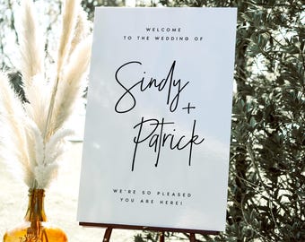 May include: White wedding welcome sign with black text. The sign reads "Welcome to the wedding of Sindy + Patrick. We're so pleased you are here!"