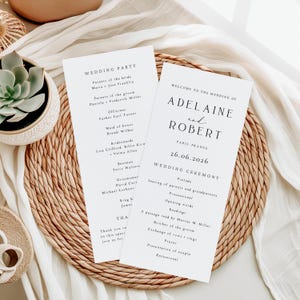 May include: Two white wedding ceremony programs with black text, featuring the names Adeline and Robert, and the date June 26, 2026. The programs list the wedding party and ceremony details. The programs are on a woven placemat.
