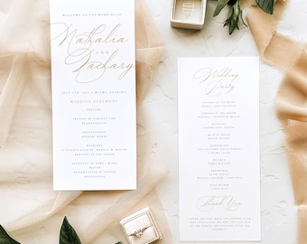 May include: Elegant wedding stationery featuring gold script on white paper. The design includes a wedding ceremony program and a wedding party list. A ring box and a ring are also visible, along with decorative fabric and greenery.