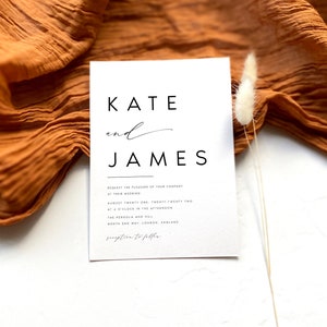 May include: A minimalist wedding invitation in white, with the names "Kate and James" in black. The invitation includes event details and is set against a textured orange fabric and a white background, with a sprig of dried flowers.