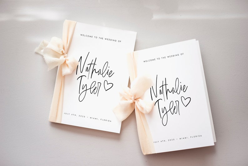 Peut inclure: Deux programmes de mariage blancs avec un ruban p&ecirc;che nou&eacute; autour. Les programmes portent le texte "Bienvenue au mariage de Nathalie Tyler" et la date "4 juillet 2030 - Miami, Floride".