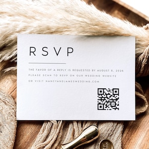 May include: A white RSVP card with black text that reads "RSVP", "The favor of a reply is requested by August 5, 2026", "Please scan to RSVP on our wedding website", and "or visit nancyandjameswedding.com". A black and white QR code is in the bottom right corner.