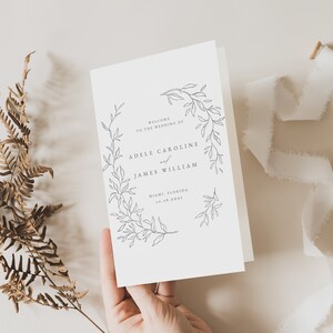 May include: A white wedding invitation with a simple floral design. The text reads "Welcome to the wedding of Adele Caroline and James William, Miami, Florida 10.08.2021".