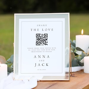 May include: A white sign with a gold frame, featuring a black and white QR code. The sign reads "Share the Love" and includes the names "Anna and Jack" with the date "10.06.2035".