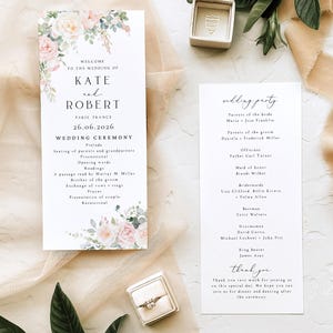 May include: Two white wedding programme cards with black serif and script text, featuring watercolour pink roses and green eucalyptus leaves. One card lists the ceremony order for Kate and Robert, while the other lists the wedding party members.