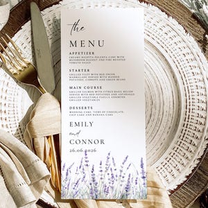 May include: A wedding menu card with the text "the MENU" at the top. The menu lists appetizers, starters, main courses, and desserts. The bottom of the card has the names "EMILY and CONNOR" and the date "26.06.2026" with a lavender floral design.