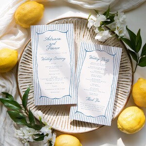 May include: Two wedding ceremony programs with blue striped borders and text, placed on a decorative plate with lemons and white flowers. The programs read "Adriana and Franco" and "Wedding Ceremony" and "Wedding Party".