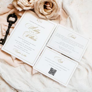 May include: White wedding invitation suite with gold accents. The main invitation card features the names "Ashley and William" in elegant calligraphy. The details card includes information about the wedding ceremony and reception. The RSVP card has a QR code for guests to RSVP online.