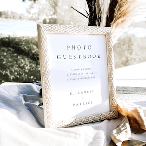 May include: A white sign with a wooden frame, with the text "PHOTO GUESTBOOK" and instructions for guests to take a photo, place it in the book, and leave a message for Elizabeth + Patrick.