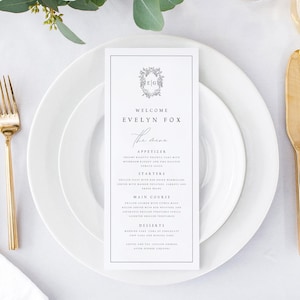Puede incluir: Una tarjeta de menú de boda blanca con un borde negro y un monograma floral gris. El texto dice "Bienvenido Evelyn Fox El Menú" y enumera los aperitivos, los entrantes, el plato principal, los postres, el café y el té, y los licores después de la cena.