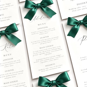 May include: A collection of white rectangular wedding menu cards featuring black printed text and a dark emerald green satin ribbon bow attached to the top of each card. The menus list courses including appetizer, starter, main course, and desserts.