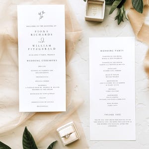 Può includere: Set di partecipazioni di nozze con un anello in una scatola, due biglietti bianchi con testo nero e verde. I biglietti mostrano i dettagli del matrimonio e i nomi degli invitati.