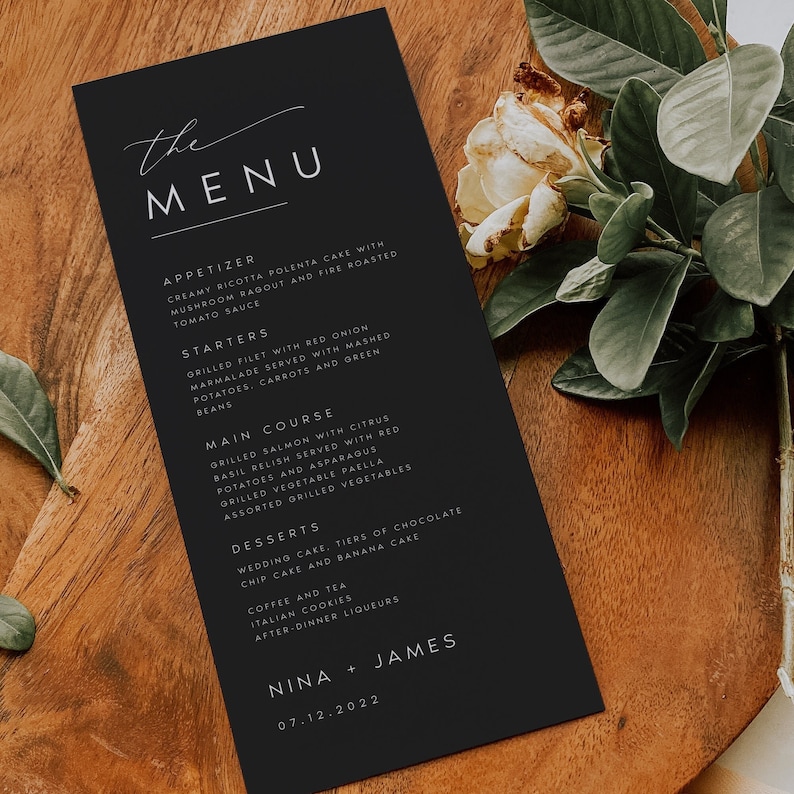 May include: Black and white wedding menu with the word "the MENU" in a script font. The menu lists appetizers, starters, main course, desserts, and coffee and tea. The bottom of the menu has the names "NINA + JAMES" and the date "07.12.2022".