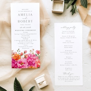 May include: Two white wedding programme cards with black serif and script text, featuring a vibrant floral illustration of pink, orange, and red flowers at the bottom. Includes a small beige ring box with a ring and an empty beige jewellery box.