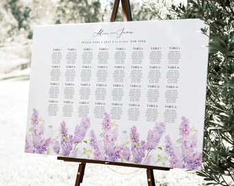 Op de afbeelding: Een witte trouwzittingkaart op een ezel, met een bloemenontwerp van paarse bloemen aan de onderkant. De kaart bevat gastennamen onder tabelnummers. De bovenkant van de kaart heeft de namen "Alice en James" en de datum.