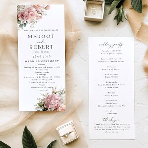 May include: Two white wedding programme cards with black text and pink floral illustrations. One card lists the ceremony order for Margot and Robert, while the other lists the wedding party. A small ring box with a ring and an empty box are included.