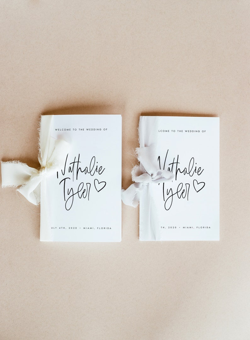 Peut inclure: Deux programmes de mariage blancs avec du texte noir. Les programmes sont li&eacute;s avec un ruban blanc. Le texte indique "Bienvenue au mariage de Nathalie Tyler" et comprend la date et le lieu du mariage.