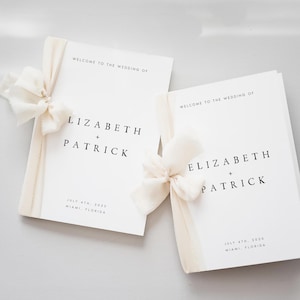 Könnte beinhalten: Zwei weiße Hochzeitskarten mit dem Text "WELCOME TO THE WEDDING OF LIZABETH + PATRICK" und dem Datum "JULY 4TH, 2020 MIAMI, FLORIDA". Jede Karte ist mit einem cremefarbenen Band und einer Schleife gebunden.