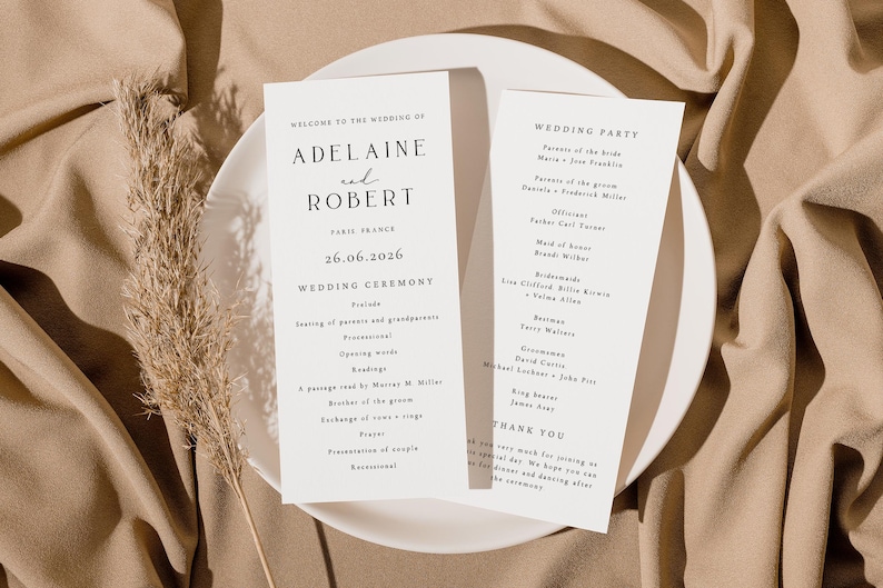 May include: Two elegant wedding ceremony programs on a white plate, featuring the names "Adelaine and Robert" and the date "26.06.2026". The program details the ceremony and wedding party. A dried plant stem adds a natural touch.