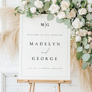 May include: White wedding welcome sign with black text. The sign reads "M|G"  "Welcome to our wedding" "Madelyn and George" "24.08.2021 London, England"