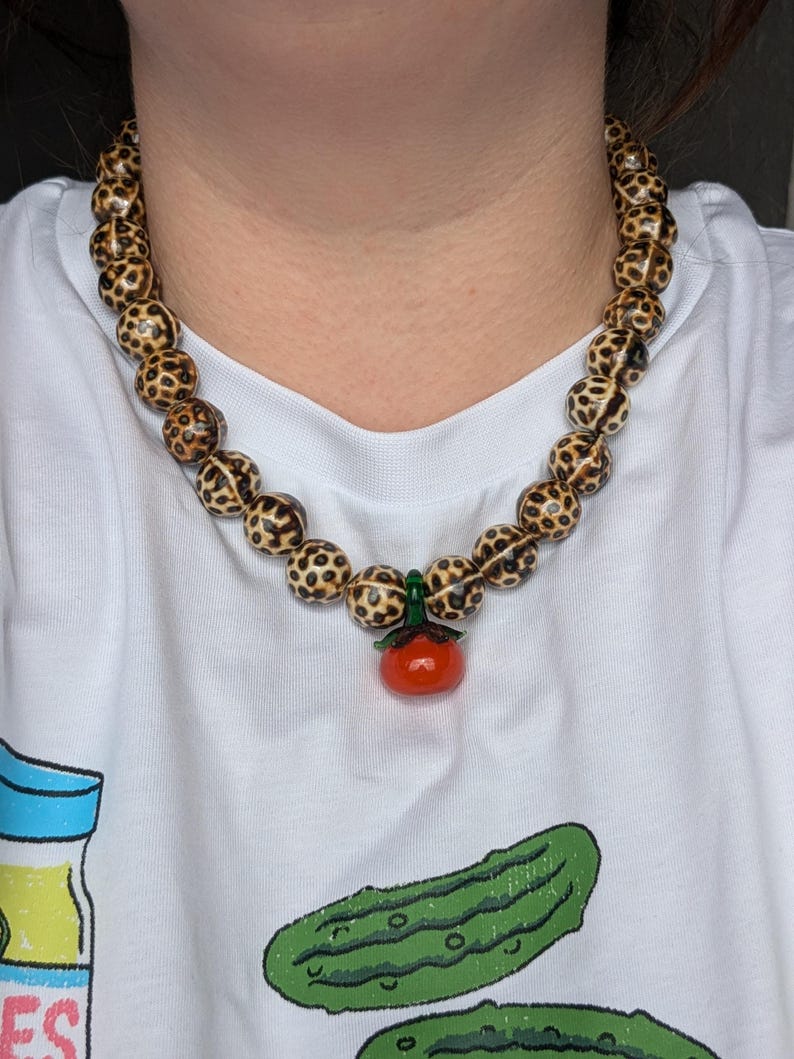 TOMATINA - Statement Necklace Leopard Ceramic Beads & Glass Tomato Pendant – Bold Summer Jewelry – Handmade Necklace – Playful Gift
Round ceramic beads in a wild leopard print radiate fierce vibes, while the glossy tomato-shaped glass pendant adds an unexpected, pop of juicy charm. A true statement piece that doesn’t take itself too seriously: ideal for confident looks with a sense of humor, sultry Italian summer nights, or anyone who loves to wear their passion and wild side with a wink.