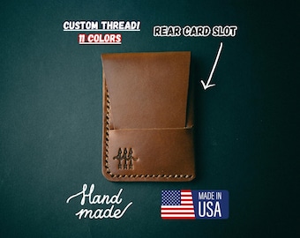 May include: A brown leather wallet with a rear card slot. The wallet is hand-stitched and has the text "Hand made" and "Made in USA" printed on it.