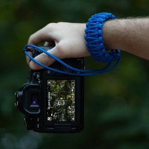 May include: A black DSLR camera with a blue camera strap. The camera screen displays "No card in camera".