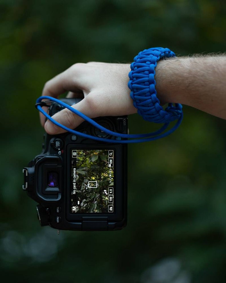 May include: A black DSLR camera with a blue camera strap. The camera screen displays "No card in camera".