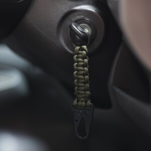 May include: A green paracord keychain with a black metal carabiner clip attached to a car key.