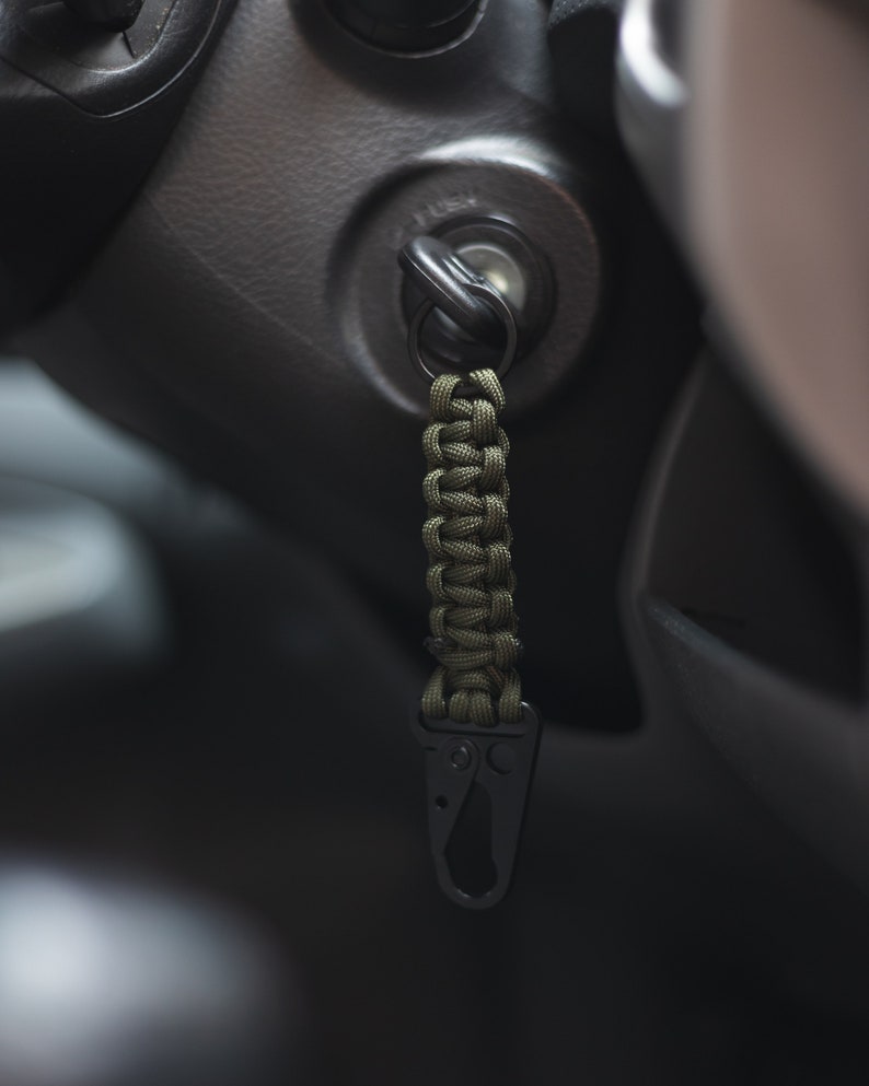 May include: A green paracord keychain with a black metal carabiner clip attached to a car key.