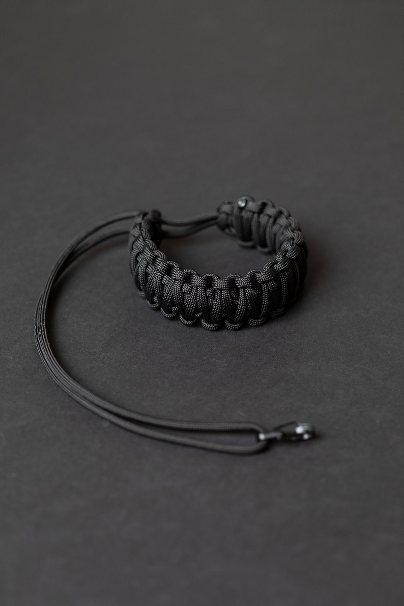 May include: A black paracord camera strap with a braided design and a metal clasp.