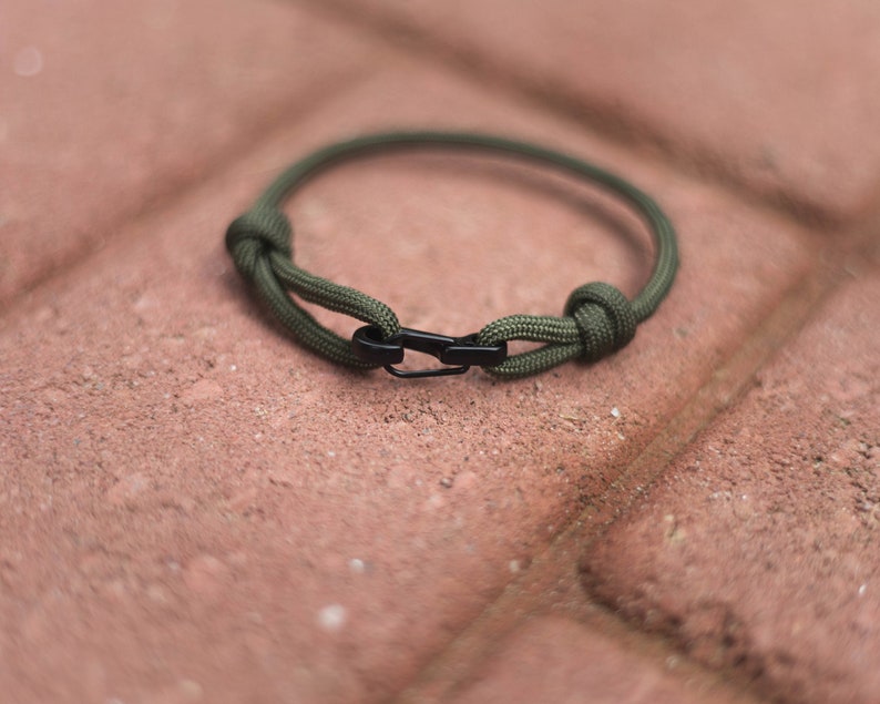 Pode incluir: Um bracelete de paracord verde com um fecho de metal preto.