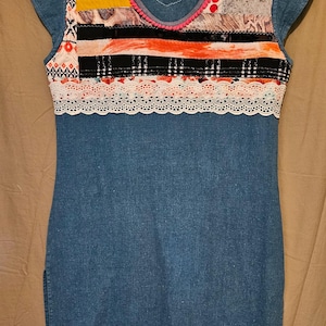 May include: A blue denim dress with a colorful patchwork design on the top. The dress has a white lace trim and a white fringe hem.