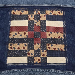 May include: A blue denim jacket with a patchwork quilt design on the back. The quilt is made of various fabrics with red, white, and blue colors. The quilt is surrounded by a lace trim.